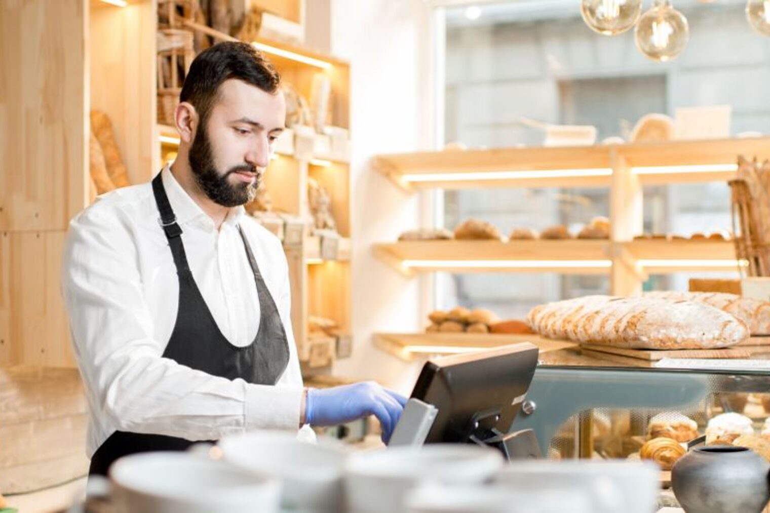 Bäckerei-Verkäufer gibt Geldbetrag in Kassensystem ein. Bäckerei-Verkäufer gibt Geldbetrag in Kassensystem ein.