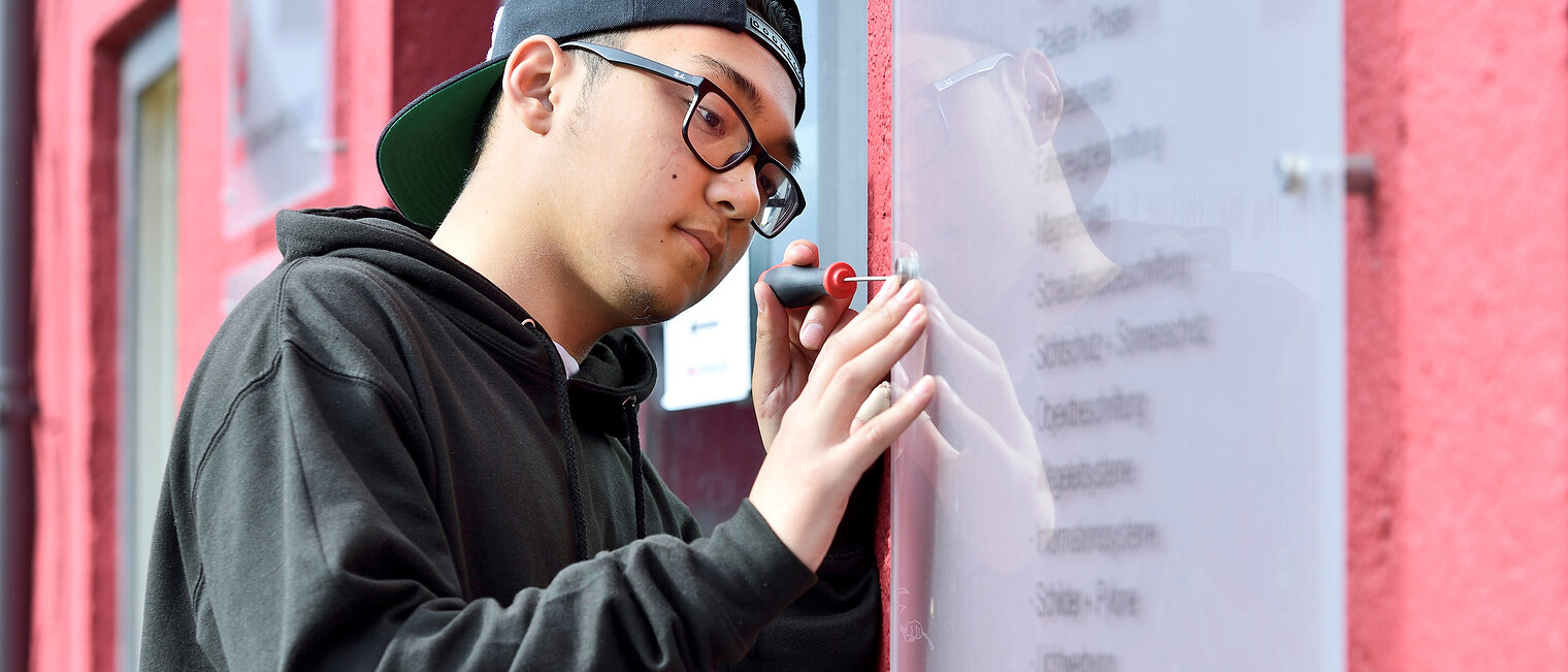 Ein junger Mann des Schilder- und Lichtreklame-Handwerks arbeitet an einer Schautafel.